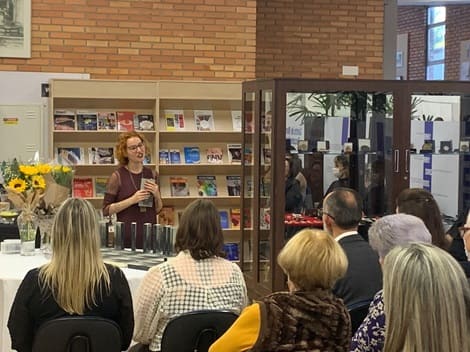 Foto do lançamento de algum livro com a escritora falando para um grupo de pessoas.